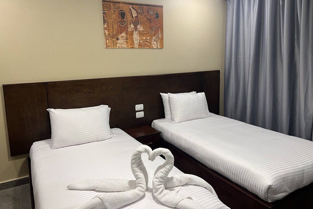Una habitación de hotel con dos camas individuales, un cabecero oscuro, una obra de arte colgada en la pared y una cortina gris.