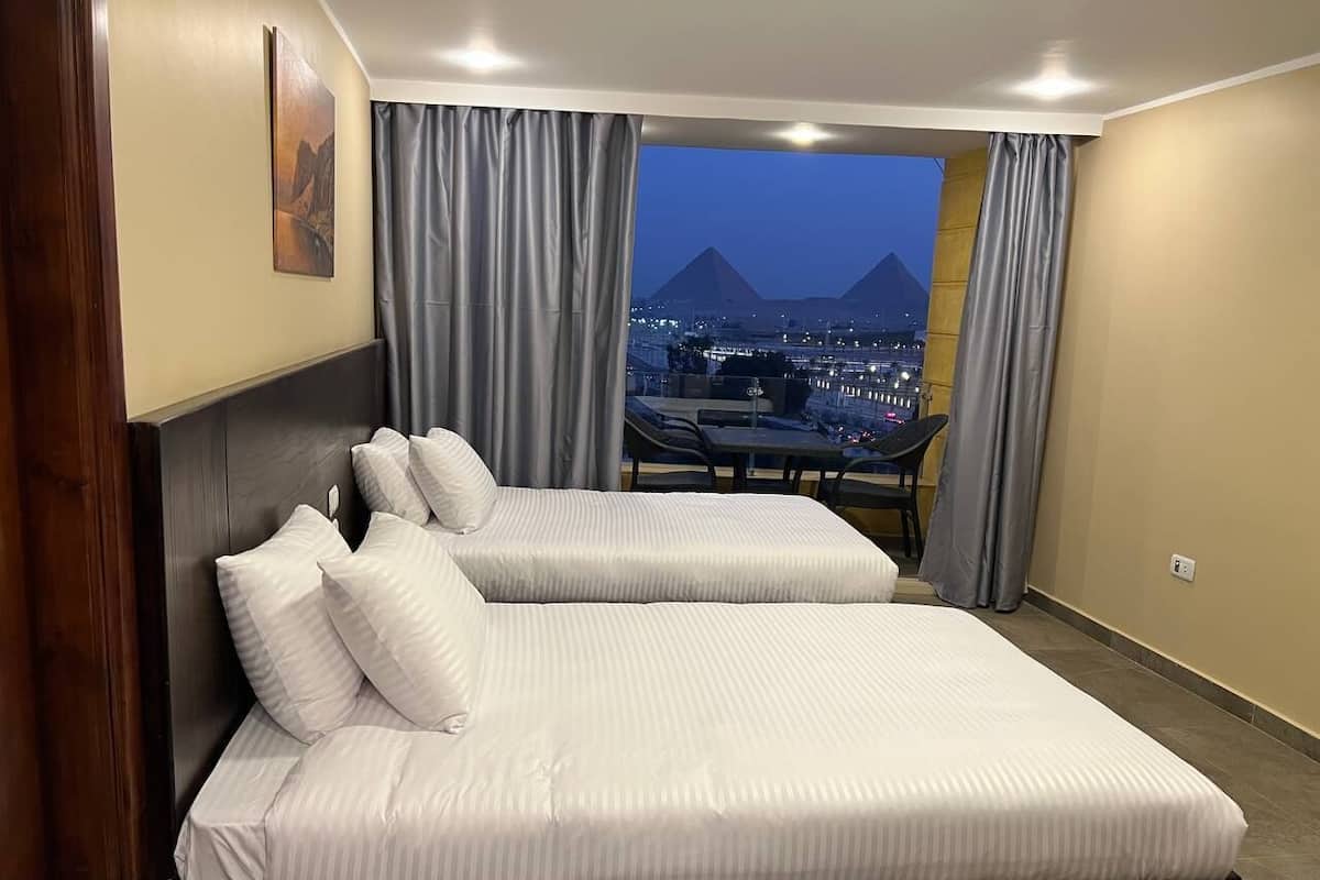 Habitación de hotel con dos camas y vista a una ciudad y montañas al anochecer.