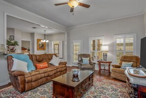 Relax in this traditional living room with a leather sofa, armchair, and coffee table, surrounded by a patterned rug and ceiling fan.
