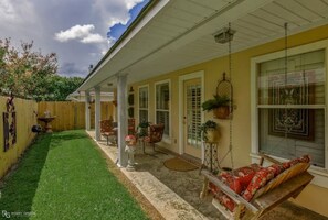 Relax in a serene outdoor space with a swing, table, and chairs, surrounded by a well-manicured lawn and a small fountain.
