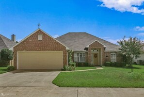 Stunning single-story home with a front porch and garage door, set amidst a beautifully manicured lawn.