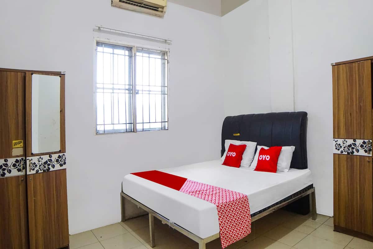 A single-bed room with a wooden wardrobe, a mirror, a window with bars, and an air conditioning unit.