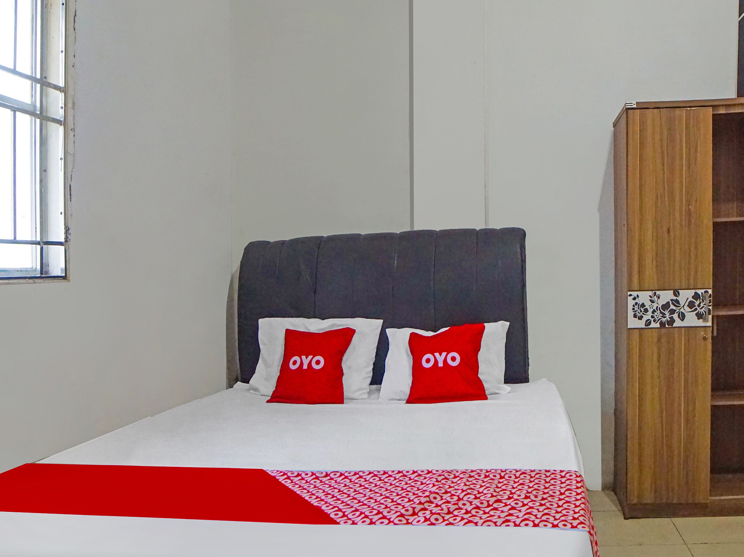 A bed with two pillows labeled "OYO," a wooden wardrobe, and a window with blinds.