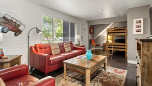 Una sala de estar acogedora con un sofá de cuero rojo, una mesa de centro de madera y una cama individual en el fondo.