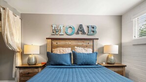 Un dormitorio con cama, dos mesitas de noche, cabecero de madera y un cartel en la pared que dice "MOAB".