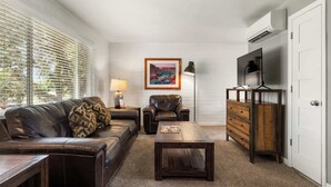 A living room with a leather sofa, a wooden coffee table, a wooden dresser, a framed picture on the wall, and a TV on a stand.