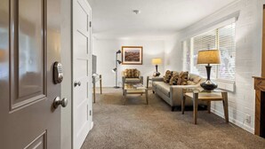 A living room with a sofa, coffee table, and lamps. There is a door with a keypad lock and a framed picture on the wall. - Hot Tub Under the Stars • Fire Pit • Downtown (Moab)