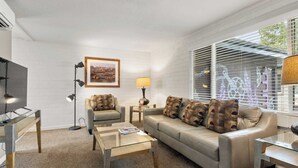 A modern living room with a sofa, coffee table, and lamp. There is a framed picture on the wall and a window with blinds. - Hot Tub Under the Stars • Fire Pit • Downtown (Moab)