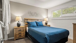 A bedroom with a bed, two bedside tables, a wall-mounted light fixture, a window with blinds, and a wall decoration of bicycles. - Hot Tub Under the Stars • Fire Pit • Downtown (Moab)