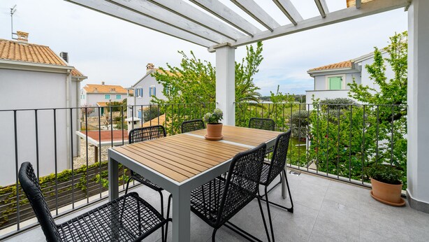 Ein Balkon mit Holztisch und -stühlen, Blumentöpfen und Blick auf benachbarte Häuser.