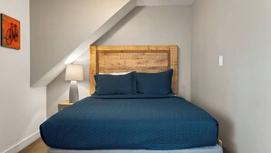Camera da letto con una testiera in legno, una coperta trapuntata blu, una lampada da comodino e un quadro appeso alla parete.
