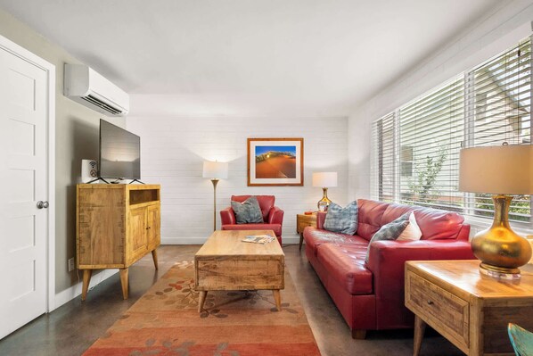 Ein Wohnzimmer mit einem roten Sofa, einem Holztisch und einem Fernseher auf einem Schrank.
