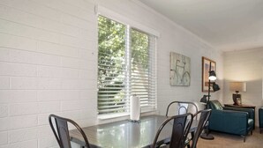 A dining area with a table and chairs, a window with blinds, a lamp, and a couch.