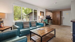A living room with a blue sofa, wooden coffee table, and a lamp. There is a window with blinds, a door, and a cabinet.