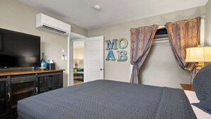 A hotel room with a bed, a flat-screen TV, a dresser, and a wall-mounted air conditioner.