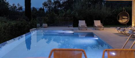 A modern outdoor pool area with lounge chairs and a hanging chair, surrounded by greenery.