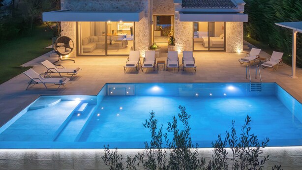 Una casa moderna con piscina, area salotto esterna e facciata in pietra.