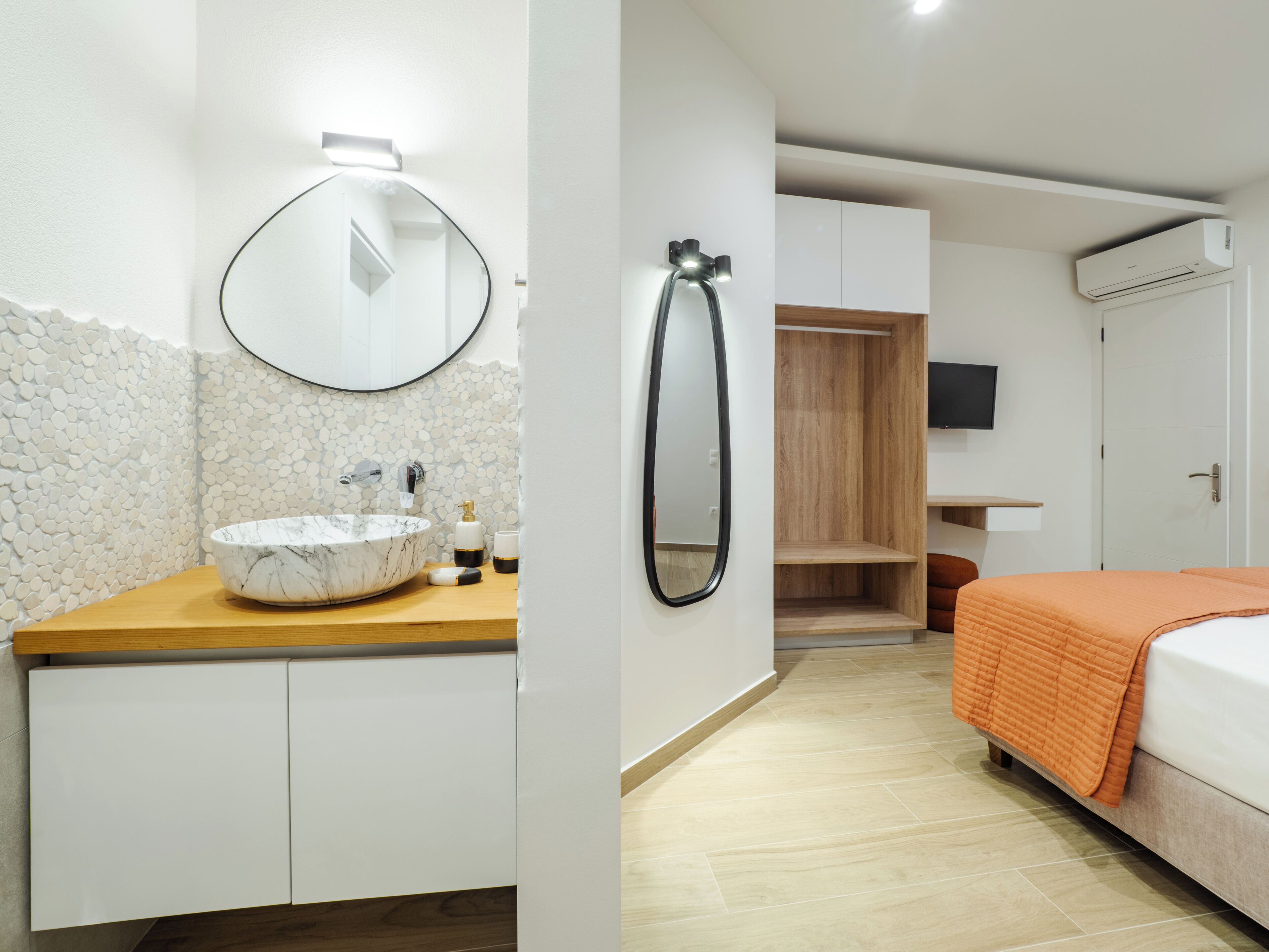 A modern bathroom with a marble sink, a round mirror, and a wooden vanity.
