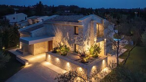Una casa moderna con facciata in pietra, vialetto lastricato e illuminazione esterna.