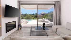Un soggiorno moderno con televisione a schermo piatto, un divano, un tavolino da caffè e vista su piscina e area relax all'aperto.