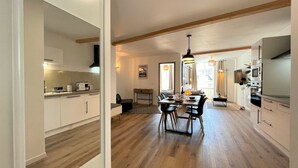 A modern kitchen with wooden flooring, white cabinetry, and a dining area with a table and chairs.