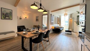 A modern kitchen with a built-in oven, a dining area with a wooden table and black chairs, and a cozy living space with a sofa and a coffee table.