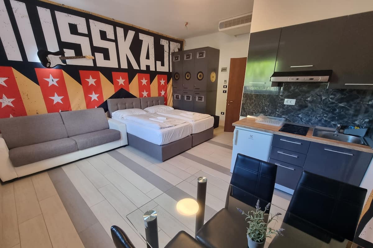 A modern living room with a sofa, a bed, a kitchen area, and a wall with a large 'SKAJ' sign.