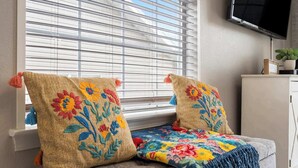 Un rincón acogedor con un sofá y dos cojines decorativos con motivos florales, una manta de colores y un televisor montado en la pared.