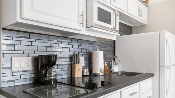 Una cocina moderna con gabinetes blancos, encimera negra, cafetera, bloque de cuchillos y dispensador de toallas de papel.