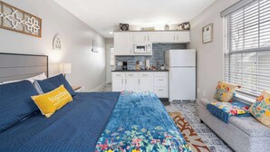 Un dormitorio pequeño con cama, un sofá y una kitchenette al fondo.
