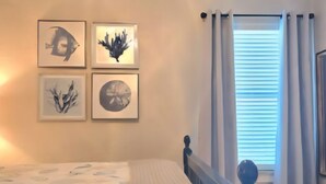 A bedroom with a bed, a window with curtains, and four framed artworks on the wall. - Paradise Vibes! 4-bedroom house in welcoming Bolivar Peninsula! (Bolivar Peninsula)