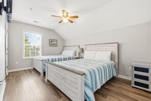 Une chambre avec deux lits, un ventilateur de plafond, une fenêtre avec des stores et un radiateur.