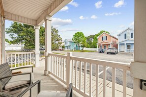 A covered porch with wicker furniture, a view of a street with houses, and a clear sky. - 2 Bed, 2 Bath Coral Cottage—Walk to the Beach! (Myrtle Beach)