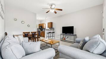 Ein Wohnzimmer mit einer Couch, einem Couchtisch, einem Fernseher und einem Deckenventilator.