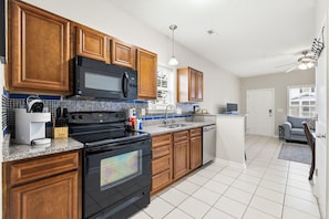 A modern kitchen with wooden cabinets, a black stove, a microwave, and a sink. - 2 Bed, 2 Bath Coral Cottage—Walk to the Beach! (Myrtle Beach)
