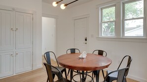 Un espace repas comprenant une table ronde en bois, six chaises et des luminaires suspendus.