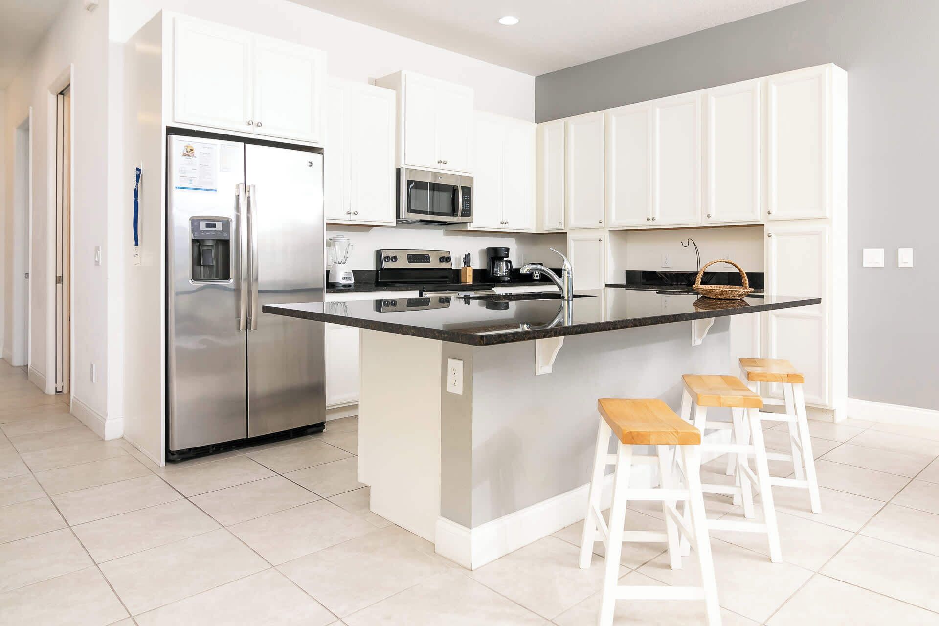 Una cocina moderna con armarios blancos, electrodomésticos de acero inoxidable, una encimera negra y taburetes de madera.