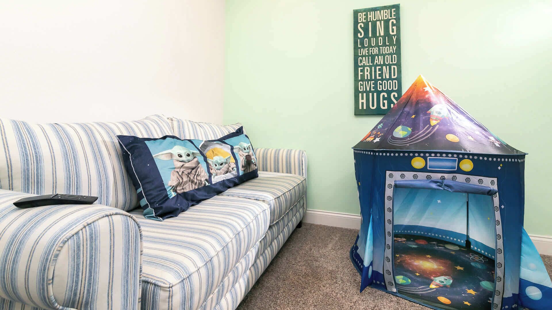 Un sofá a rayas con dos almohadones, uno con un personaje, y una pequeña tienda de juegos con temática espacial.