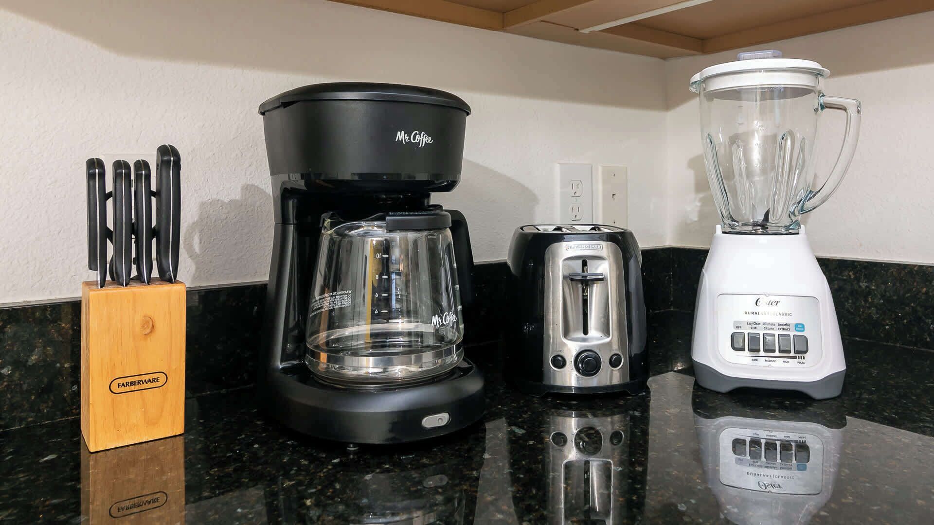 Una encimera de cocina con cafetera, tostadora, licuadora y un bloque de cuchillos.