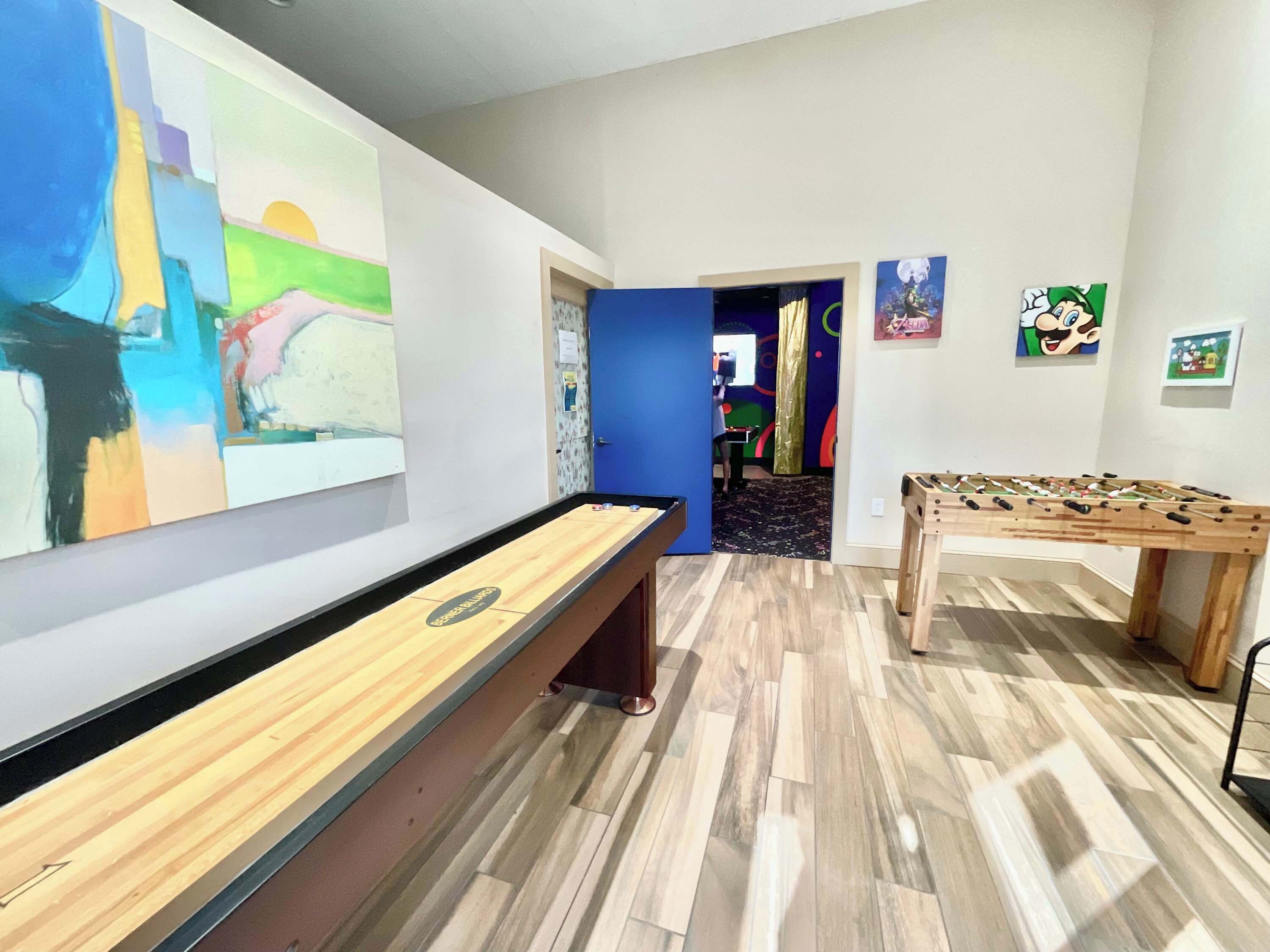 A room with a foosball table, a pool table, and a large abstract painting on the wall.