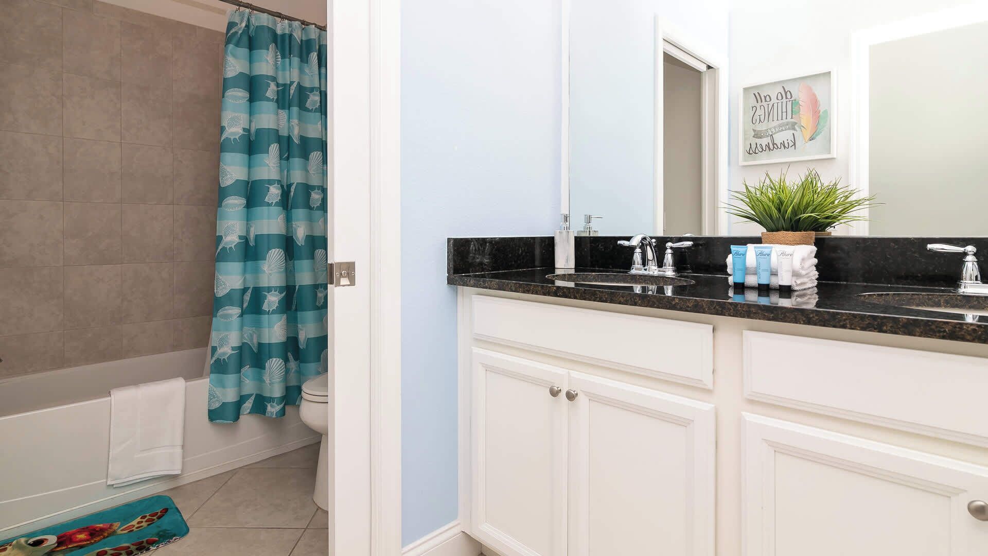 Une salle de bain avec une baignoire, un rideau de douche orné de motifs représentant des créatures marines, un lavabo avec un plan de travail noir et un miroir agrémenté d’une décoration.
