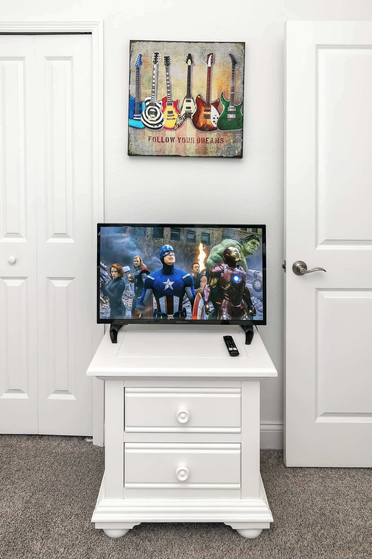 A television on a white cabinet with a superhero movie playing.