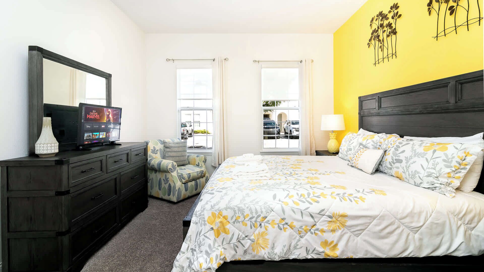 A hotel room with a bed, a TV, a chair, and a window.