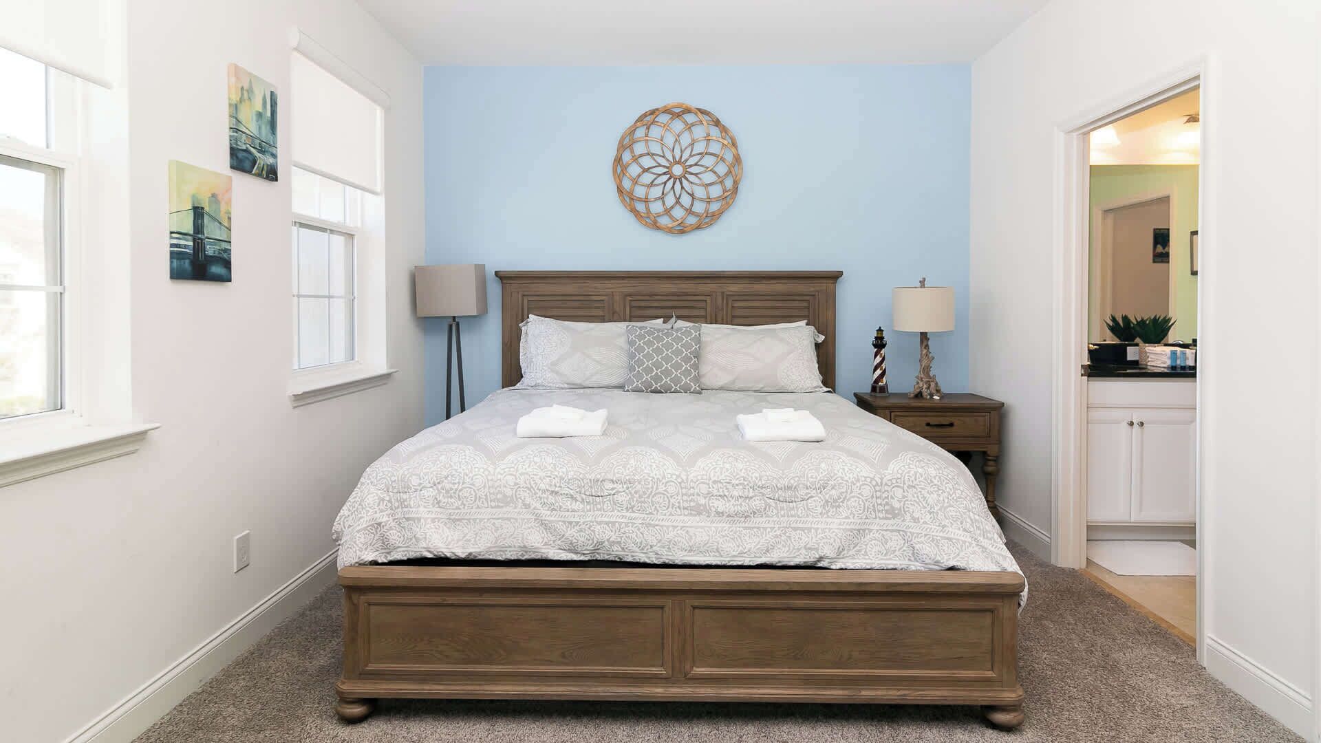 A bedroom with a large bed, two bedside lamps, a decorative wall piece, and a view into the bathroom.