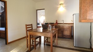 Un coin repas avec une table et des chaises en bois, un ventilateur de plafond, une cuisine avec des placards en bois et un réfrigérateur.