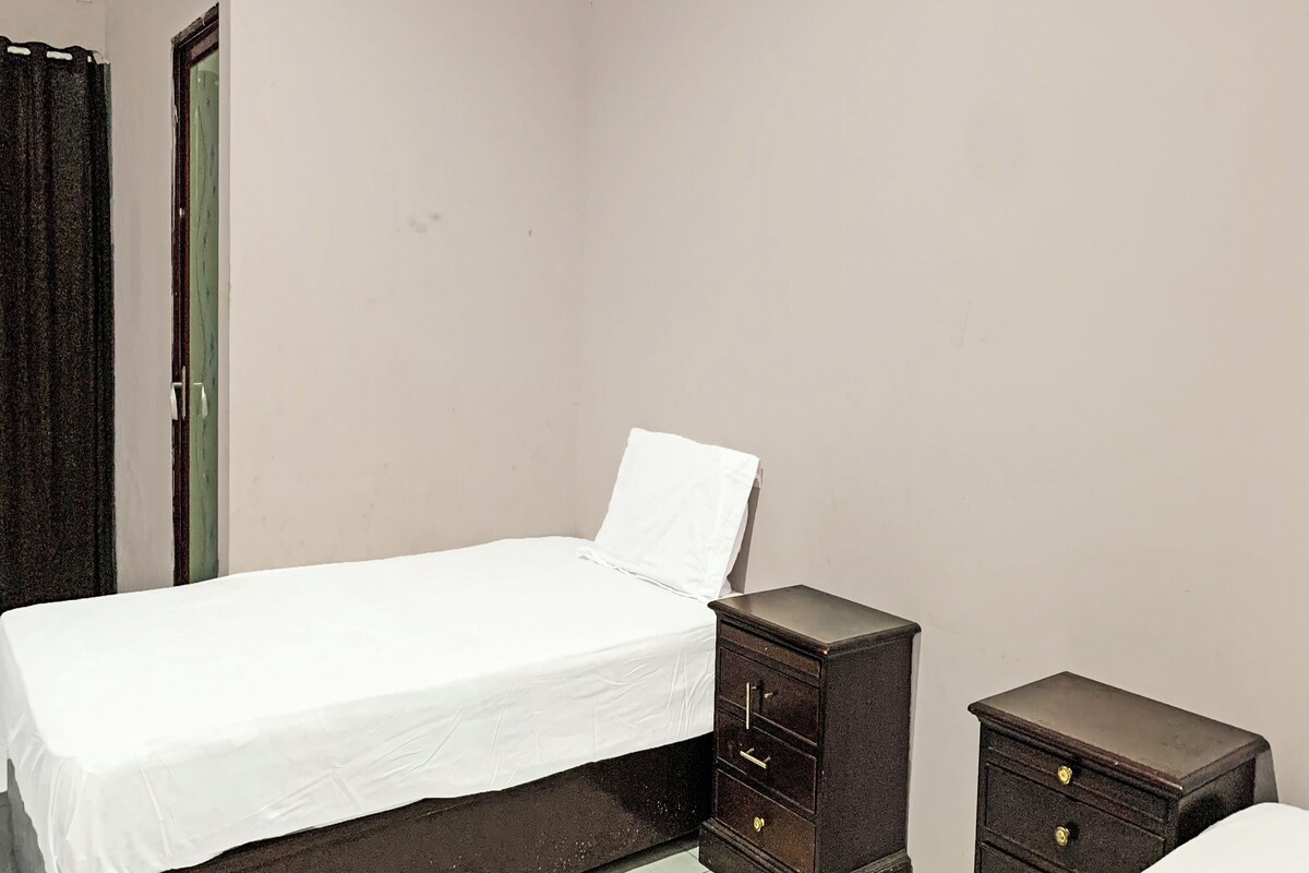A single bed with a white sheet, a small wooden nightstand with drawers, and a dark-colored wardrobe.