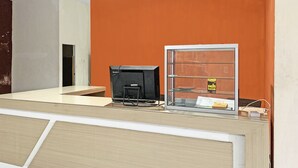 Uma receção com balcão, uma televisão de ecrã plano, uma vitrine de vidro e uma mesa pequena com régua de tomadas.