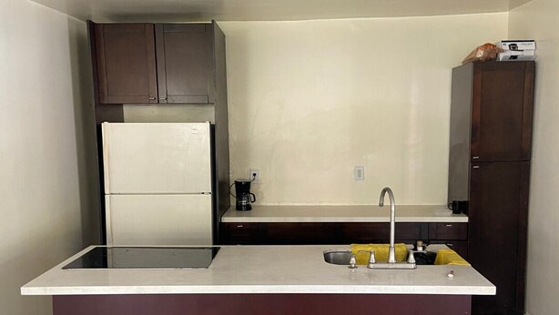 A compact kitchen with a central island, a built-in refrigerator, and dark wooden cabinets. - Eco-Shared Hype  (Miami)