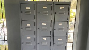 A row of grey metal storage lockers with labels, positioned against a wall with a window. - Eco-Shared Hype  (Miami)