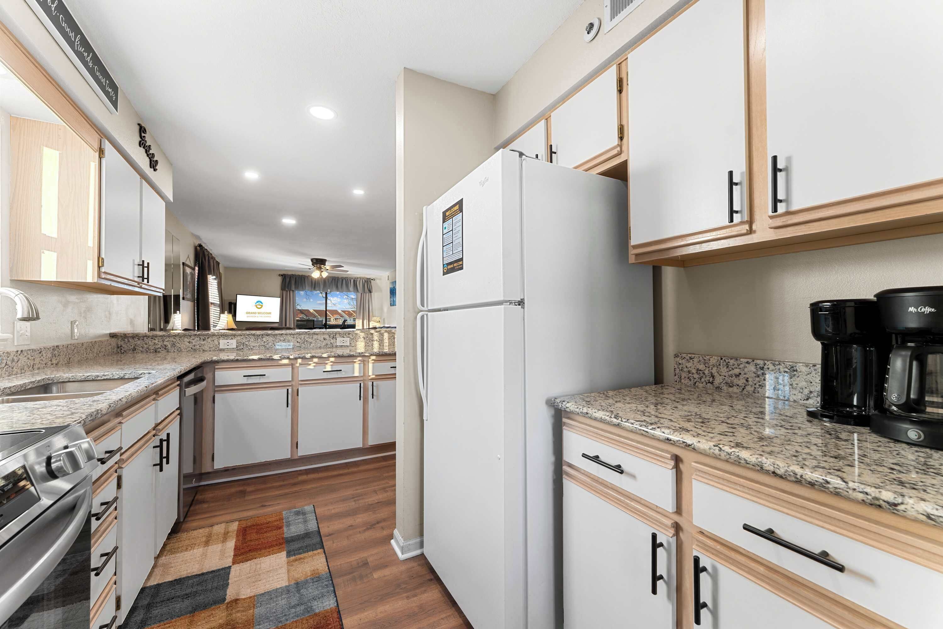 A modern kitchen with white cabinets, a granite countertop, a refrigerator, and a coffee maker.